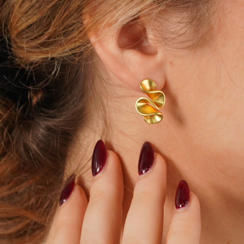 Twyla Earrings, an 18K gold plated 925 silver earring, shown worn on an ear with a hand touching the face.