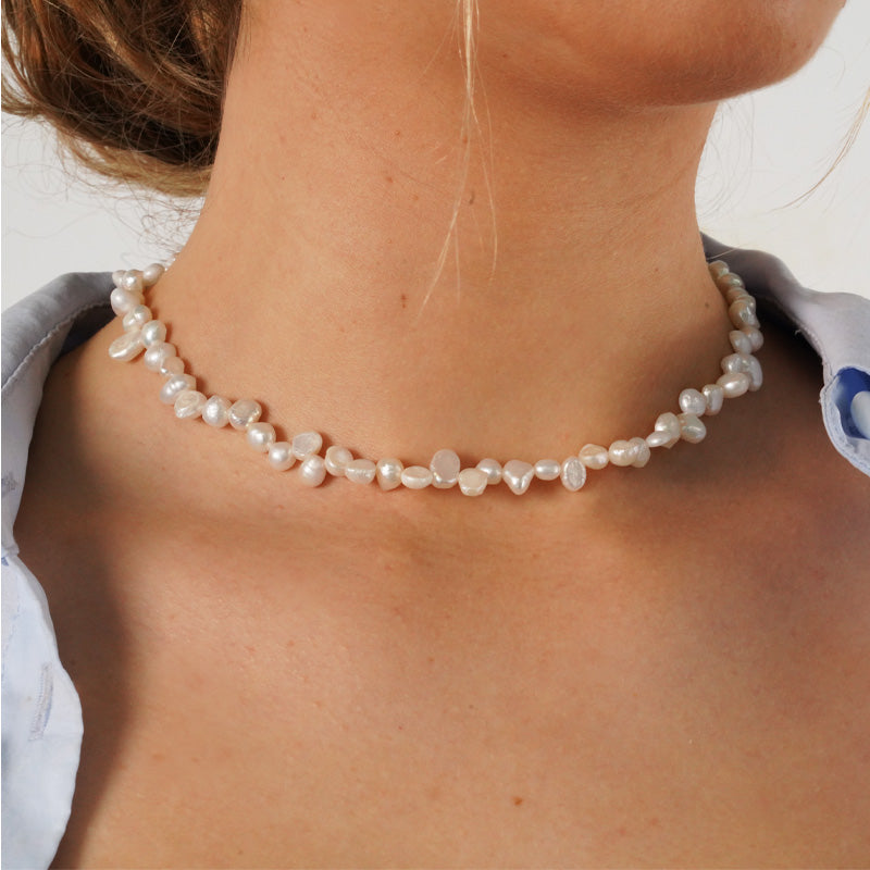 Elyse Pearls necklace, a 14K gold plated stainless steel necklace with irregular freshwater pearls, shown on a model's neck.