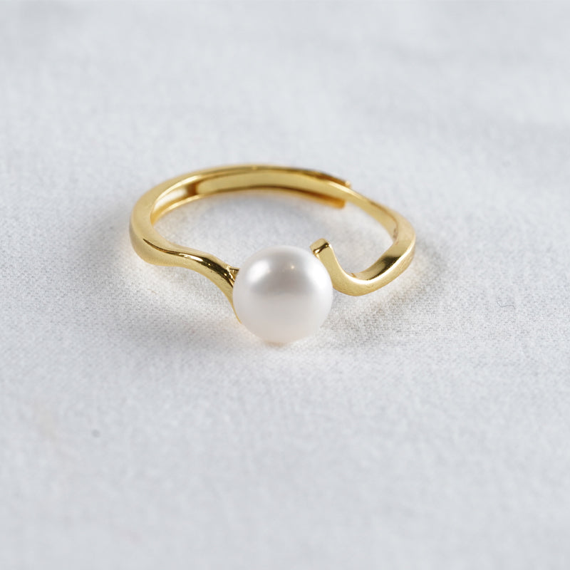 Ebb and Pearl Ring, an 18K gold plated 925 silver ring with a white pearl, shown at an angle on fabric.